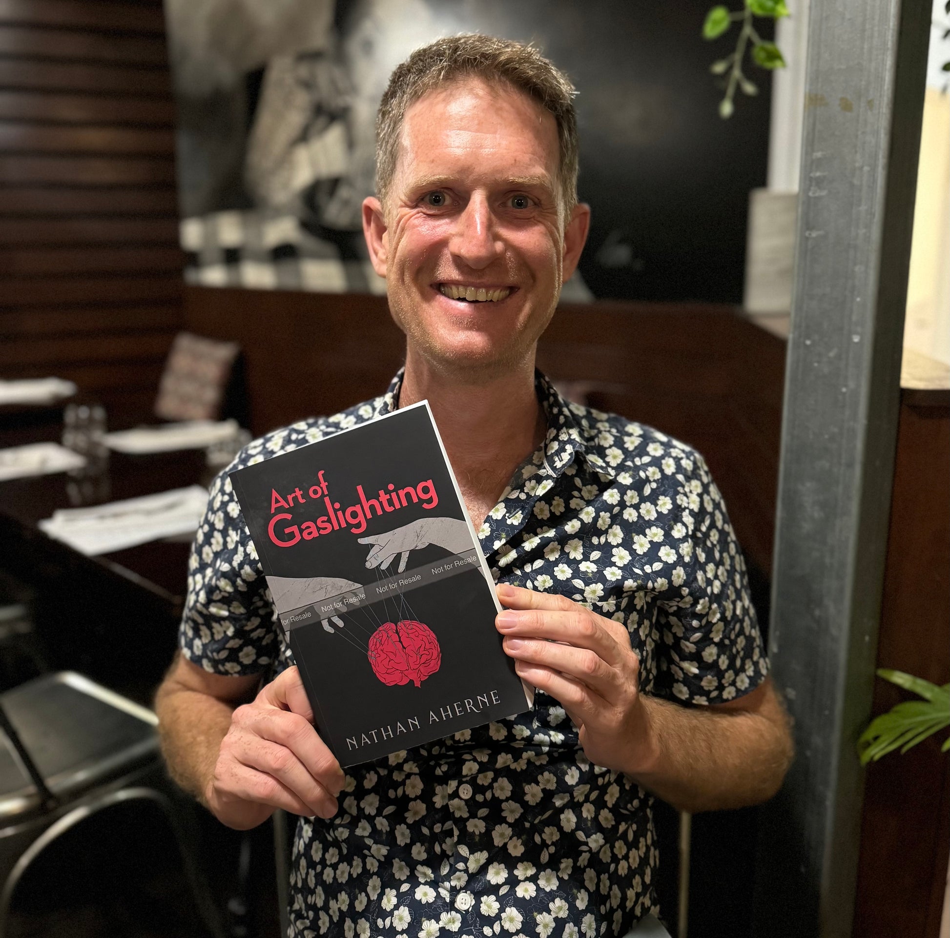 Nathan at dinner holding Art of Gaslighting author proof version